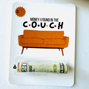 May include: A white card with a cartoon orange couch and the text "MONEY I FOUND IN THE C.O.U.C.H."  A rolled up dollar bill is visible in a clear plastic pouch on the card.