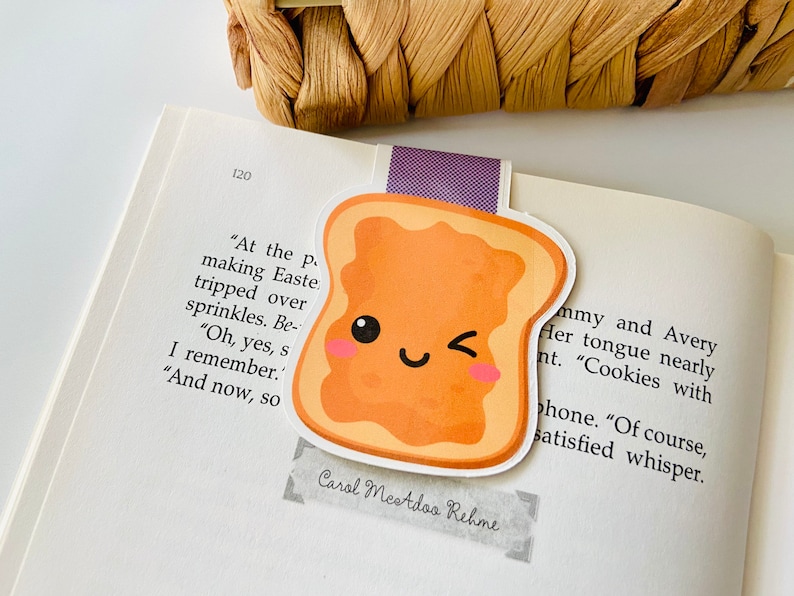 May include: A cute cartoon bookmark shaped like a slice of toast with peanut butter. The toast has a smiling face with a wink and rosy cheeks. The bookmark is on a page of a book with text that reads "At the p making Easte tripped over sprinkles. Be- "Oh, yes, s I remember. "And now, so Carol Mestdoo Rehme mmy and Avery Her tongue nearly nt. "Cookies with phone. "Of course, satisfied whisper."