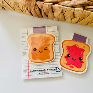 May include: Two magnetic bookmarks shaped like slices of toast. One slice has peanut butter and the other has strawberry jam. Both have cute cartoon faces.