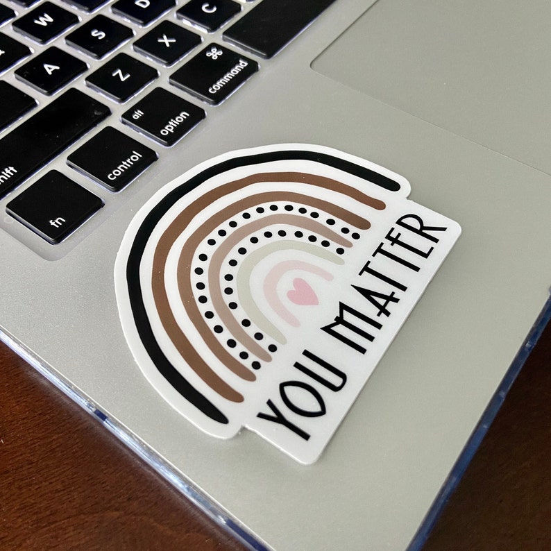 May include: A sticker with a rainbow design in shades of brown, beige, and pink with a small heart at the center. The text "You Matter" is written in black lettering on a white background.