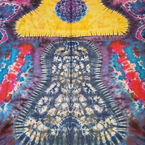 May include: A vibrant tie-dye textile featuring a symmetrical design with a large yellow shape at the top. The pattern incorporates shades of blue, purple, red, and brown, creating a psychedelic and artistic aesthetic. The fabric appears to be cotton or a similar material.
