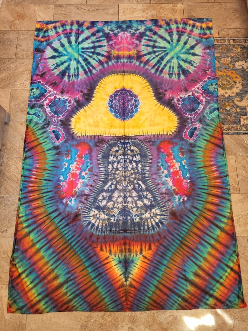 May include: A vibrant tie-dye textile featuring a kaleidoscope of colors. The design includes concentric patterns in shades of blue, purple, yellow, orange, and green. The central motif is a symmetrical, cloud-like shape with intricate details.