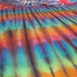 May include: A vibrant tie-dye textile featuring a spectrum of colors, including orange, red, blue, and green. The design has a striped pattern with dark brown lines. The fabric appears to be spread out, with a section of blue and white tie-dye in the background.
