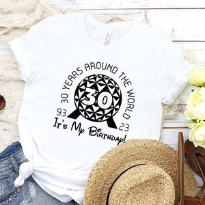 May include: White t-shirt with a black graphic of the Spaceship Earth ride at Epcot with the text "30 Years Around The World 93 It's My Birthday! 23"