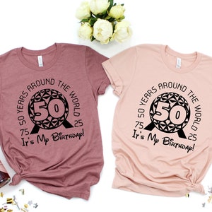 May include: Two pink t-shirts with a black graphic of the Spaceship Earth ride at Epcot with the number 50 inside. The text around the graphic says "50 Years Around the World 75 It's My Birthday! 25".