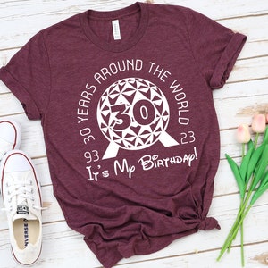 May include: A maroon t-shirt with a white graphic of the Epcot ball with the number 30 inside. The text around the ball reads "30 Years Around The World 93-23" and below the ball reads "It's My Birthday!"
