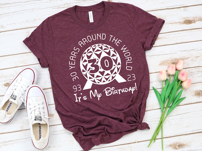 May include: A maroon t-shirt with a white graphic of the Epcot ball with the number 30 inside. The text around the ball reads "30 Years Around The World 93-23" and below the ball reads "It's My Birthday!"