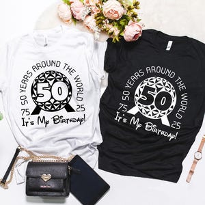 May include: Two t-shirts, one white and one black, featuring a graphic of the Spaceship Earth ride at Epcot. The graphic includes the text "50 Years Around The World It's My Birthday!"