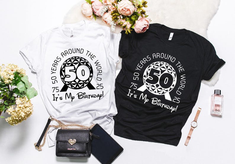 May include: Two t-shirts, one white and one black, featuring a graphic of the Spaceship Earth ride at Epcot. The graphic includes the text "50 Years Around The World It's My Birthday!"