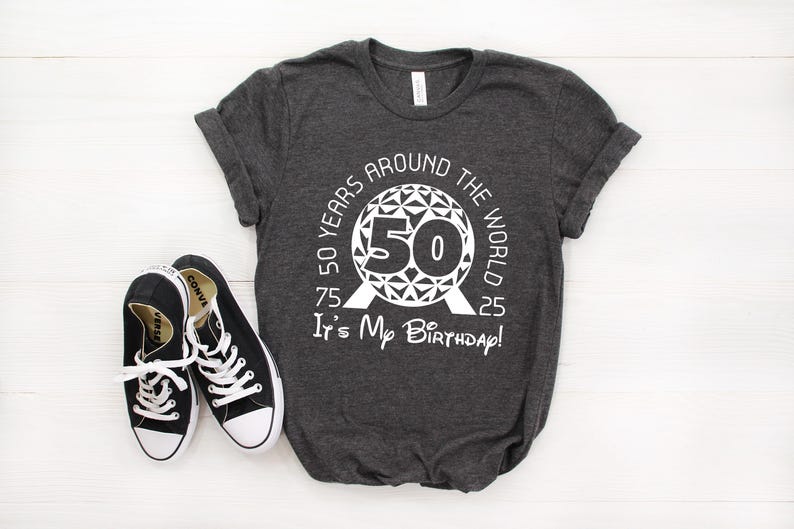 May include: A dark grey t-shirt with a white graphic of a sphere with the text "50 Years Around The World 75 50 25 It's My Birthday!" printed on it.
