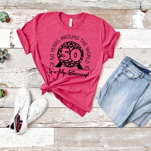 May include: A pink t-shirt with a black graphic of the Spaceship Earth ride at Epcot. The graphic includes the text "50 Years Around the World It's My Birthday!"