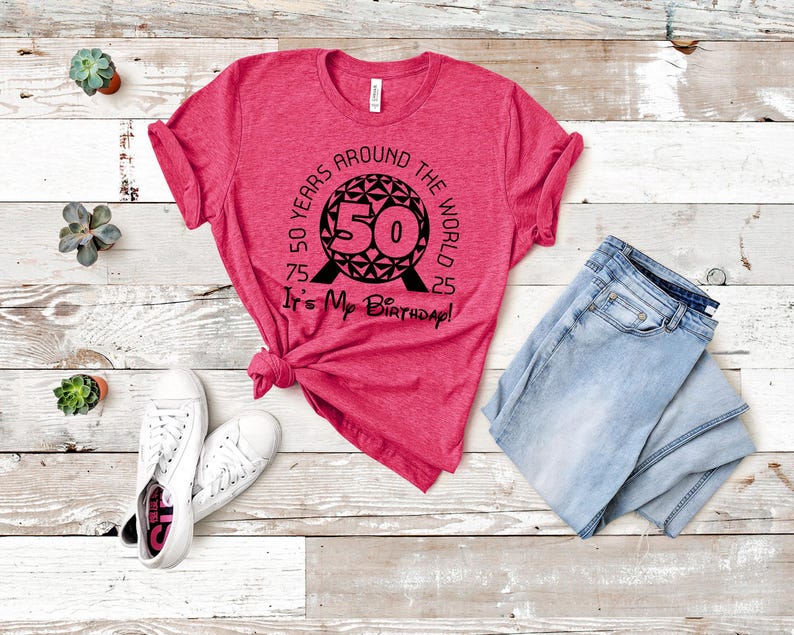 May include: A pink t-shirt with a black graphic of the Spaceship Earth ride at Epcot. The graphic includes the text "50 Years Around the World It's My Birthday!"