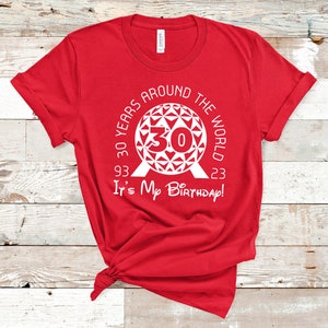 May include: Red t-shirt with a white graphic of the Epcot ball with the text "30 Years Around The World 93 - 23 It's My Birthday!"