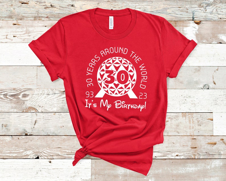 May include: Red t-shirt with a white graphic of the Epcot ball with the text "30 Years Around The World 93 - 23 It's My Birthday!"