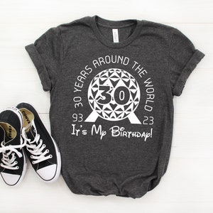May include: A dark gray t-shirt with a white graphic design featuring the Epcot Spaceship Earth icon and the text "30 Years Around The World 93 - 23 It's My Birthday!"