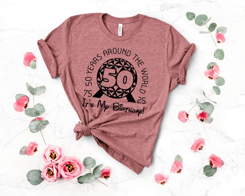 May include: A pink t-shirt with a black graphic of a sphere with the text "50 Years Around The World" and "It's My Birthday!" printed on it.
