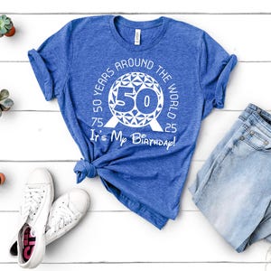 May include: A blue t-shirt with a white graphic of a 50th birthday celebration around the world. The graphic features a stylised globe with the number 50 in the centre and the text "50 Years Around The World It's My Birthday!"