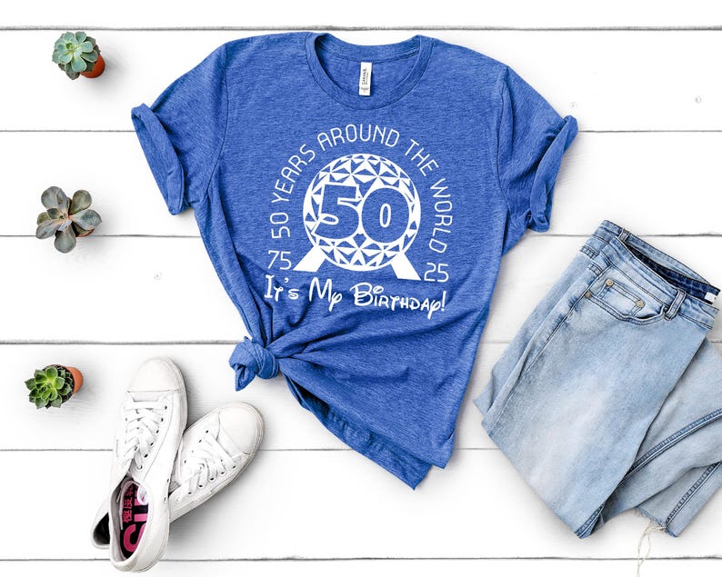 May include: A blue t-shirt with a white graphic of a 50th birthday celebration around the world. The graphic features a stylised globe with the number 50 in the centre and the text "50 Years Around The World It's My Birthday!"
