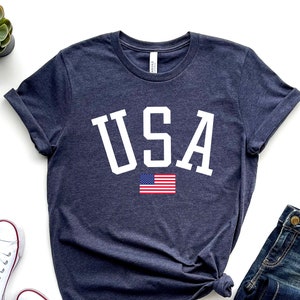 May include: A navy blue t-shirt with a white "USA" graphic and a small American flag. The shirt is made of a soft, comfortable material and has a relaxed fit.