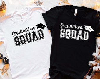 May include: Two t-shirts with the text "Graduation Squad" printed on them. One shirt is white with black text and the other is black with white text. Both shirts feature a graduation cap graphic.