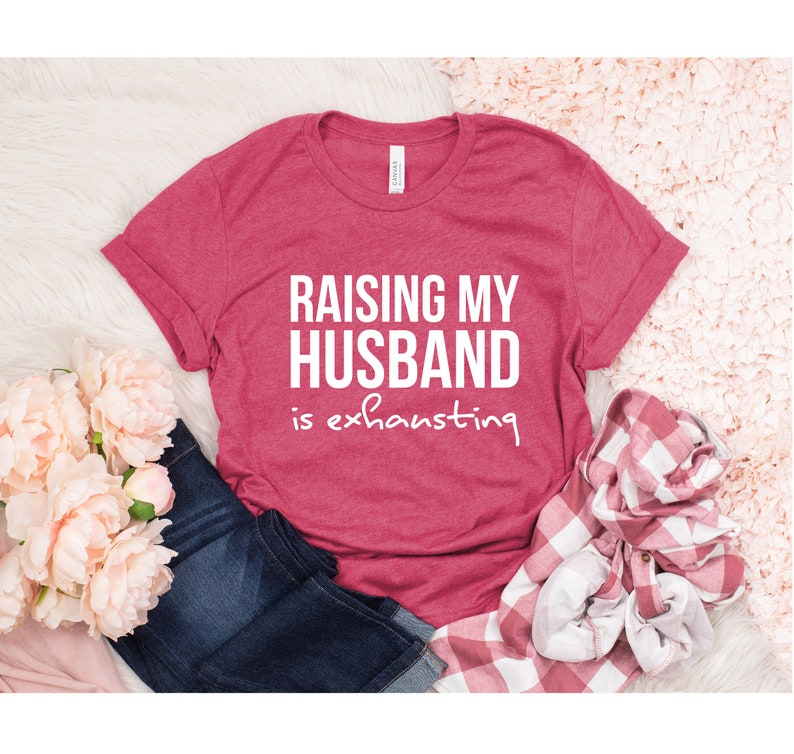 May include: A red t-shirt with the text "Raising my husband is exhausting" in white.