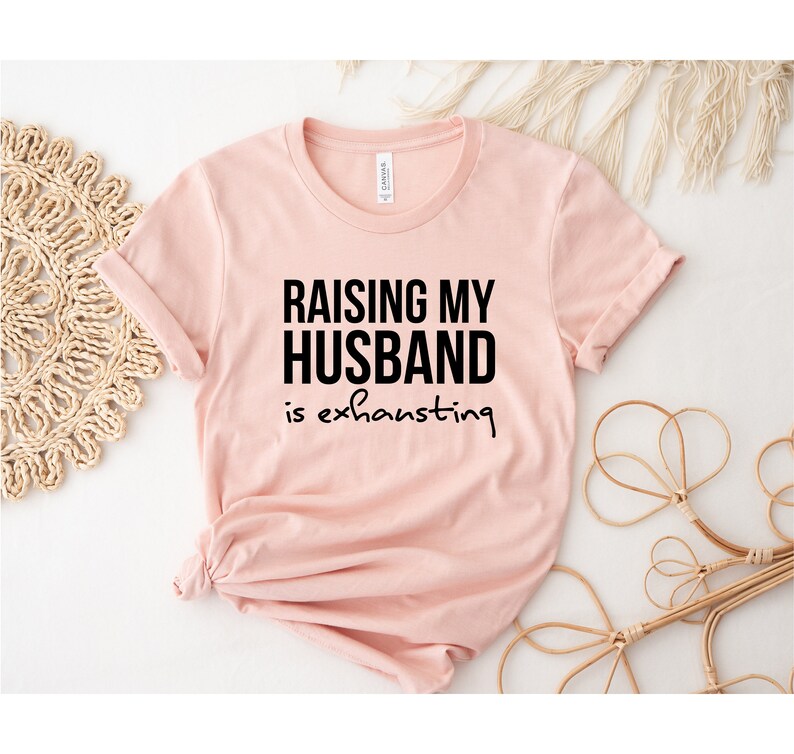 May include: A pink t-shirt with black text that reads "Raising my husband is exhausting".