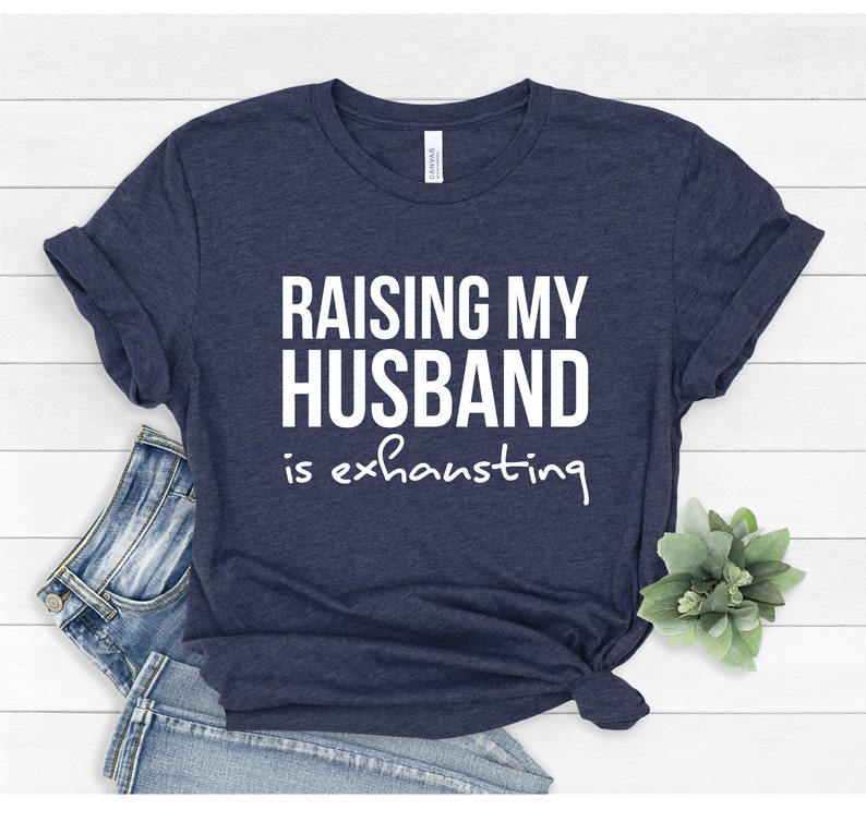 May include: A navy blue t-shirt with the text "Raising my husband is exhausting" in white.