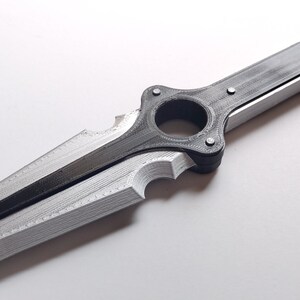 May include: A silver and black sword with a unique design. The blade is silver, and the handle and central ring are black. The sword has a distinctive shape with a circular opening near the handle and a notched edge.