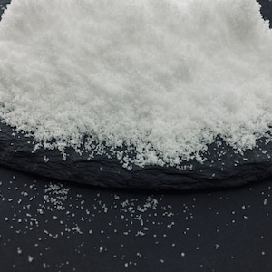 May include: A close-up of a pile of white granulated sugar on a black slate surface.