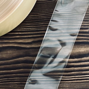 May include: A clear, transparent tape roll on a dark brown wooden surface. The tape is rolled up and has a slight sheen.