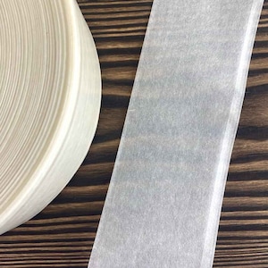 May include: A roll of white, translucent tape on a wooden surface. The tape is wound tightly and has a smooth, even texture.