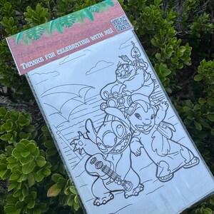 May include: A clear plastic bag containing a black and white coloring page featuring cartoon characters. The top of the bag has a brown and green design with the text "THANKS FOR CELEBRATING WITH ME!" and a QR code.