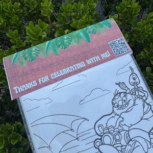 May include: A clear plastic coloring book with a brown and green decorative top. The top has the text "THANKS FOR CELEBRATING WITH ME!" and a QR code. The coloring book features a black and white cartoon illustration of characters.