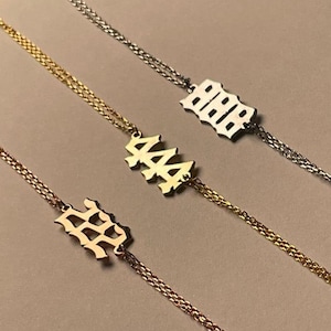 May include: Three gold chain bracelets with different numbers on the charms. The numbers are 222, 444, and 888. The charms are in a gothic font.