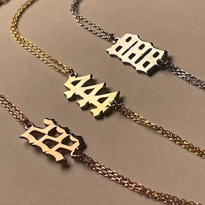 Puede incluir: Tres pulseras de cadena de oro con diferentes dijes de n&uacute;meros. Los dijes est&aacute;n en una fuente g&oacute;tica y dicen "222", "444" y "888".