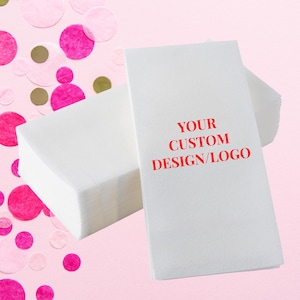 May include: White rectangular napkins with the text "YOUR CUSTOM DESIGN/LOGO" in red. The napkins are stacked on a pink background with scattered pink and gold confetti.
