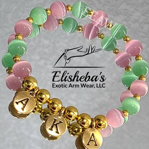 May include: A double-strand bracelet with pink and green beads and gold charms that spell out "AKA".