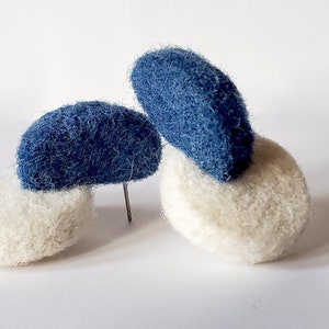 Pode incluir: Um par de brincos feitos de feltro. Um brinco é branco e tem dois círculos de feltro azul no topo. O outro brinco é branco e tem um círculo de feltro azul no topo.