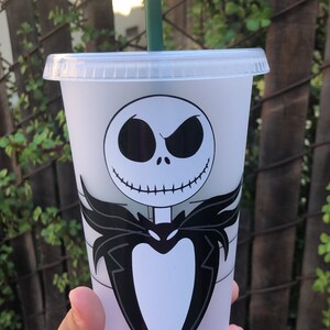 May include: A white reusable cup with a black and white image of Jack Skellington from The Nightmare Before Christmas. The cup has a green straw.