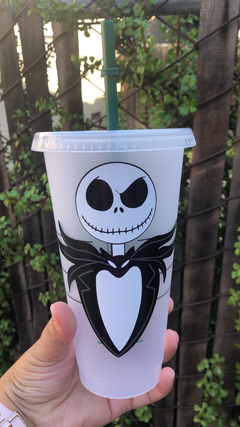 May include: A white reusable cup with a black and white image of Jack Skellington from The Nightmare Before Christmas. The cup has a green straw.