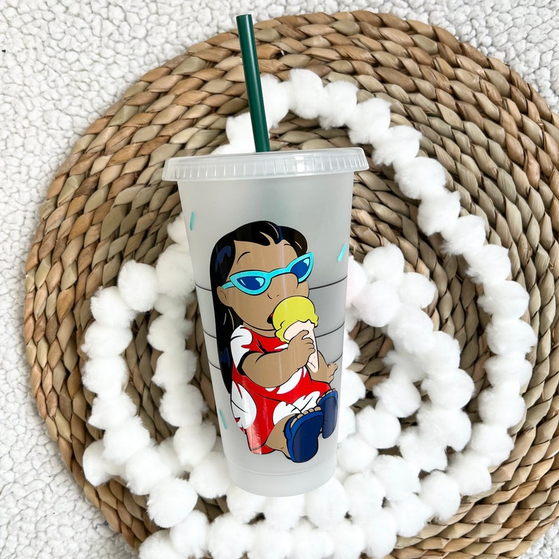 May include: A frosted clear plastic cup with a green straw. The cup has a colorful image of a cartoon character wearing sunglasses and eating ice cream. The character is wearing a red and white dress.