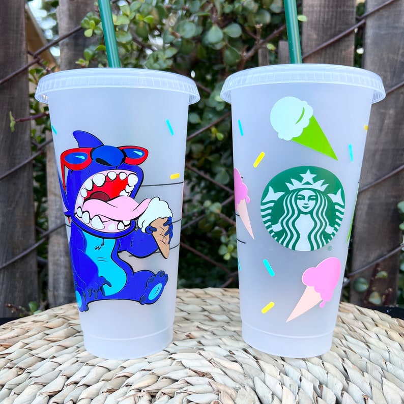 May include: Two clear plastic reusable cups with lids and straws. The cup on the left has a blue cartoon character with red sunglasses eating ice cream. The cup on the right has a green Starbucks logo and ice cream cones with pink and white ice cream.