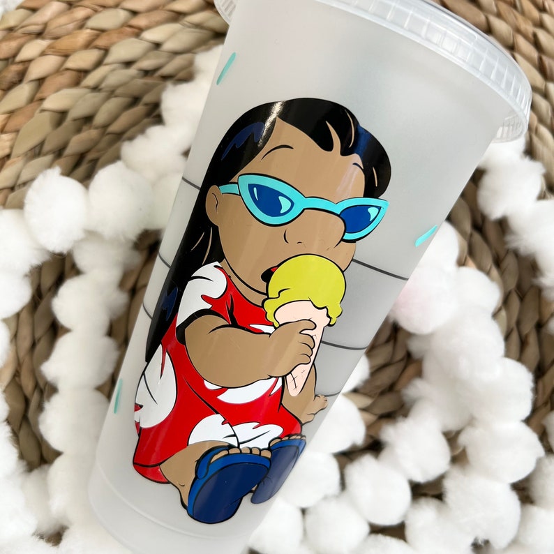 May include: A white reusable cup with a cartoon image of a girl wearing sunglasses and a red dress, holding an ice cream cone. The girl has dark hair and brown skin.