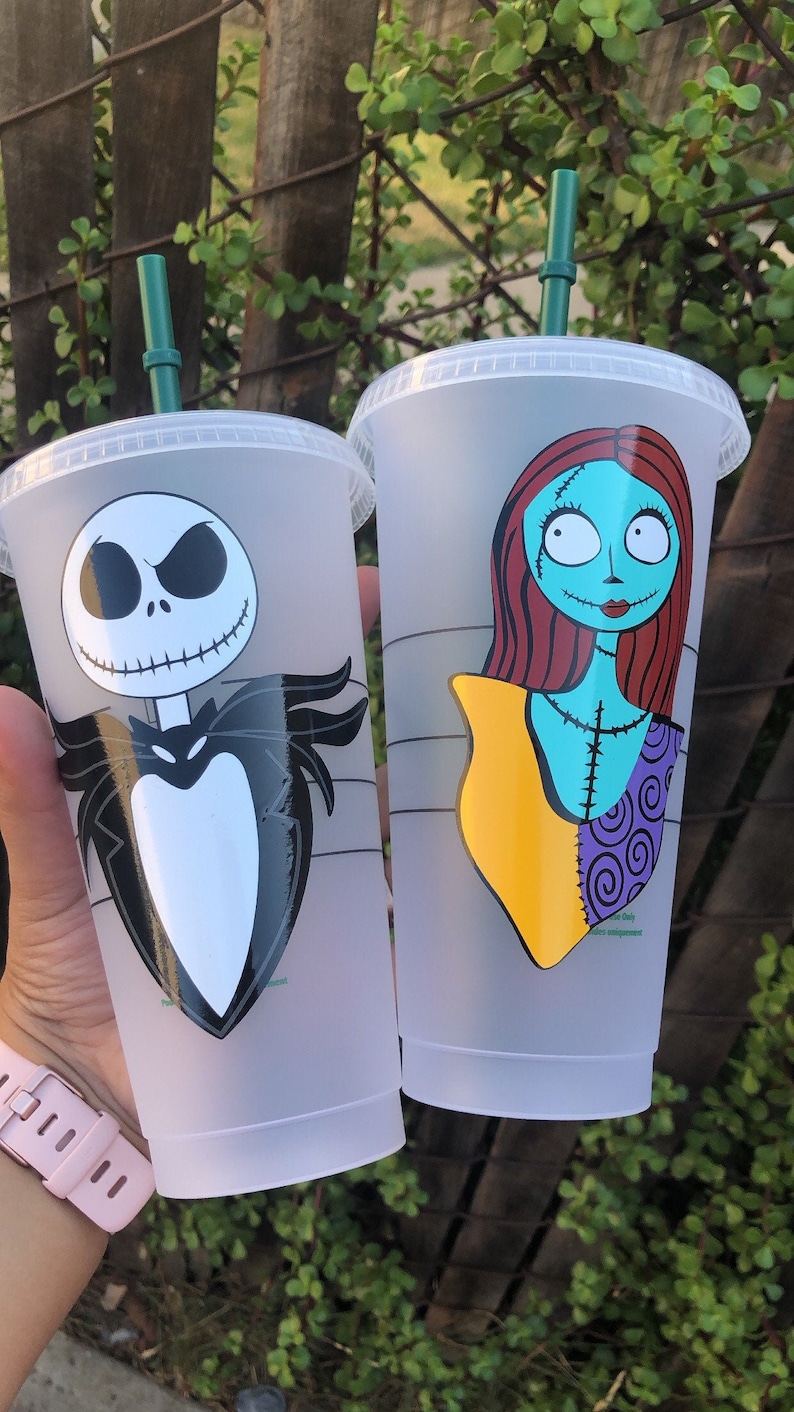 May include: Two clear plastic cups with green lids and straws. The cups have images of Jack Skellington and Sally from the Nightmare Before Christmas.