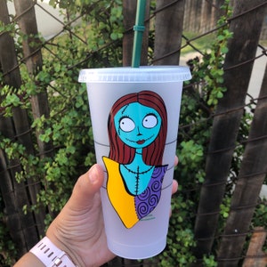 May include: A clear plastic reusable cup with a green straw. The cup has a colorful graphic of Sally from the Nightmare Before Christmas.