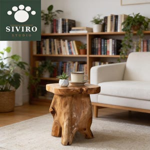 May include: A natural light brown wooden side table with a thick, organic stump-like base and a flat top surface. A small white ceramic succulent planter and a cream-colored ceramic mug on a matching saucer are placed on the table surface.