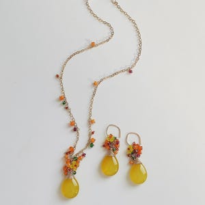 May include: A gold-toned necklace and matching earrings set. The necklace and earrings feature yellow teardrop-shaped pendants and clusters of colorful beads. The jewelry is set against a white background.