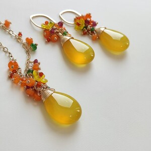May include: A jewelry set featuring a necklace and earrings. The necklace and earrings have a teardrop-shaped, yellow gemstone pendant. The pendants are accented with colorful beads and wire wrapping. The earrings have gold-colored ear wires.
