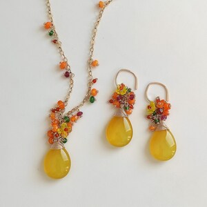 May include: A gold-toned necklace and matching earrings set. The necklace and earrings feature teardrop-shaped yellow gemstones, accented with colorful beads. The gemstones are wire-wrapped, and the jewelry is set against a white background.