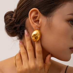 May include: A pair of large, gold-toned, round earrings. The earrings are smooth and have a slightly irregular shape.